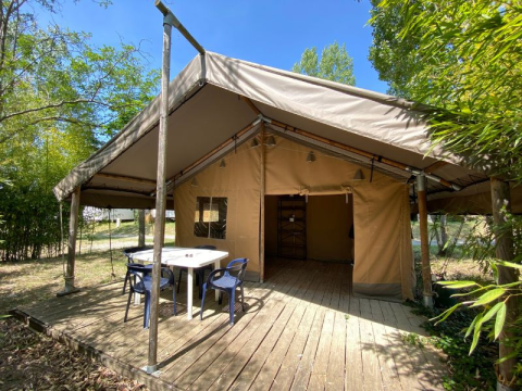 Safari-tent Lodge COSY op houten terras, met tafel en stoelen, omgeven door groen en bomen.
