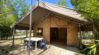Safaritent Lodge COSY met houten vlonder, zitje en tafel, omgeven door bomen en groene natuur.