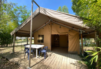 Das Safari-Zelt Lodge COSY mit Holzterrasse, Tisch und Stühlen, umgeben von grüner Natur im Sommer.