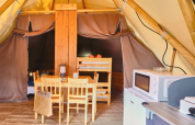 Binnenkant van een Tipi-tent bij Ludo Camping in Frankrijk met eettafel, magnetron en stapelbedden.