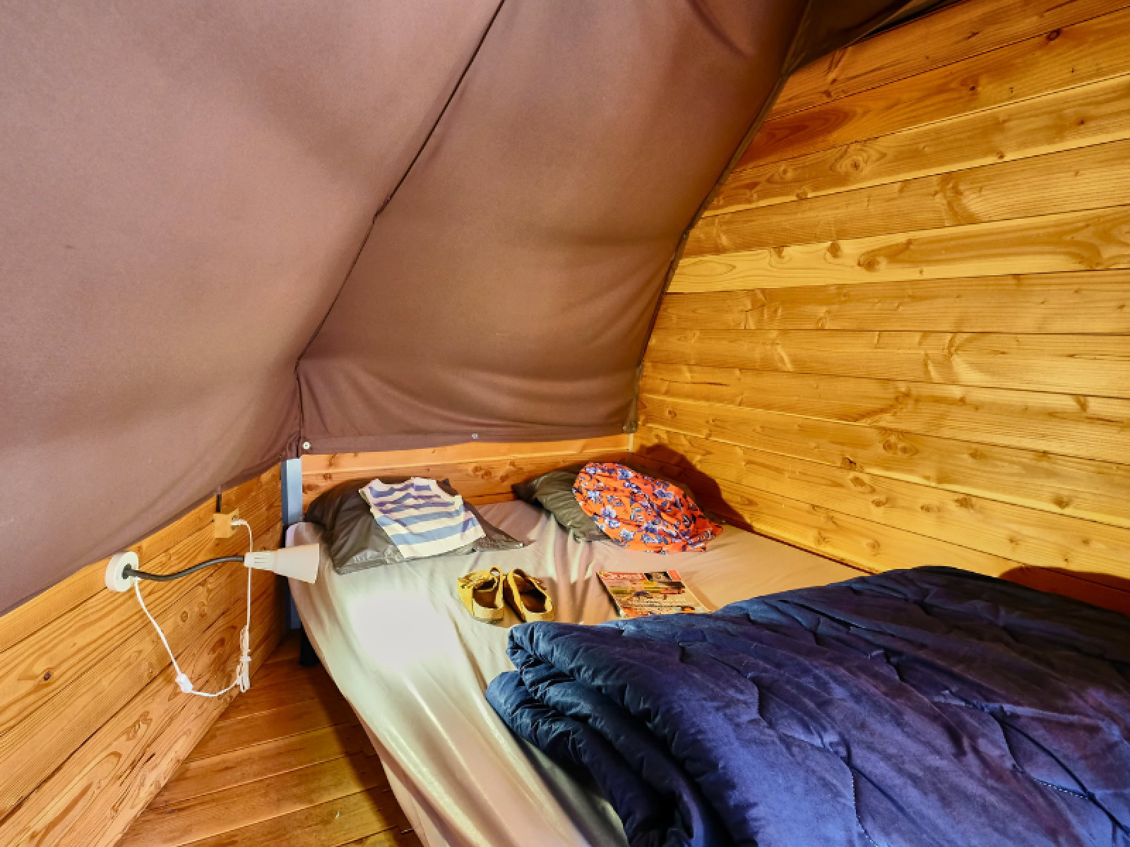 Interieur van een Tipi Tent bij Ludo Camping in Frankrijk, met bed, kussens en houten wanden.