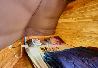 Binnenkant van een Tipi Tent bij Ludo Camping in Frankrijk, met bed, kussens en houten muren.