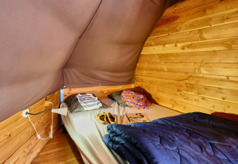 Binnenkant van een Tipi Tent bij Ludo Camping in Frankrijk, met bed, kussens en houten muren.