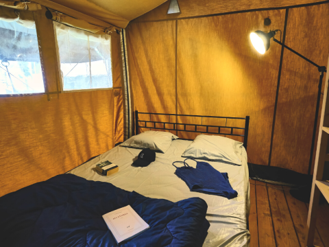 Interieur van een safaritent met bed, boek, kleding en lamp bij Lodge 'COSY' op Ludo Camping, Frankrijk.