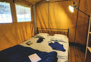 Interieur van een safaritent met bed, boek, kleding en lamp bij Lodge 'COSY' op Ludo Camping, Frankrijk.