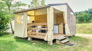 Tente safari nommée Bungalowtent, terrasse en bois, rideaux ouverts et coin cuisine dans la nature.