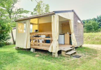 Safari tent called Bungalowtent with open curtains, wooden deck, and outdoor seating in a green field.