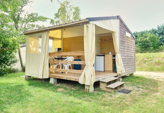 Safari tent called Bungalowtent with open curtains, wooden deck, and outdoor seating in a green field.