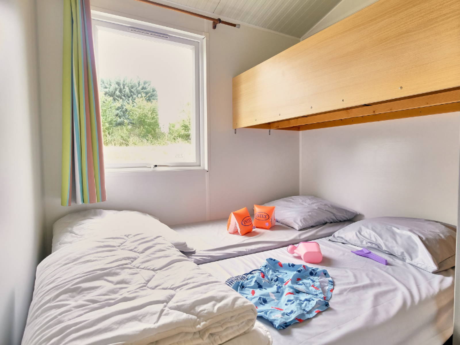 Slaapplek in Bungalowtent bij Ludo Camping in Frankrijk met stapelbed, zwemspullen en een gestreept gordijn.