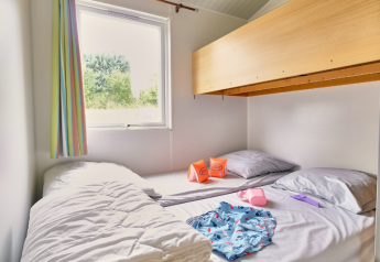 Zona de dormir en Bungalowtent en Ludo Camping en Francia, con litera, cortina de colores y accesorios de natación.