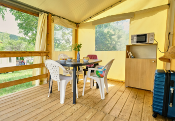 Interior de una tienda safari Bungalowtent en Ludo Camping, Francia, con mesa, sillas y estanterías.
