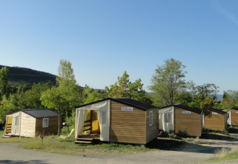 Tentes bungalows au camping Ludo en France, entourées d’arbres et de verdure sous un ciel bleu clair.