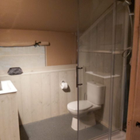 Baño en tienda safari en Ranger Lodge, Petite Suisse, Bélgica, con inodoro y ducha en la esquina.