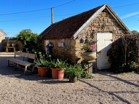 Stenhus med havekrukker og bænk under blå himmel ved La Maison Bornat i Bourgogne-Franche-Comté, Frankrig.