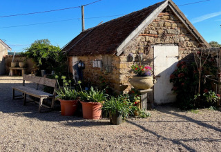 Stone building with flower pots and a bench on a sunny day at La Maison Bornat in Bourgogne-Franche-Comté, France.