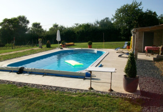 Outdoor swimming pool at La Maison Bornat holiday park, with deckchairs, greenery, and relaxing garden.