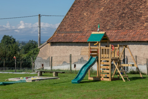 Aire de jeux avec structure en bois et toboggan sur pelouse à La Maison Bornat, Bourgogne-Franche-Comté, France.