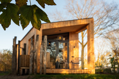 Wooden lodge Wellness Duynzicht at Sandberghe in the Netherlands, with green leaves in the foreground.
