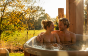 Couple relaxing in outdoor hot tub at Wellness Duynzicht, Sandberghe, Netherlands, surrounded by nature.