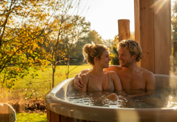 Koppel ontspant in een buitenjacuzzi bij Wellness Duynzicht, Sandberghe, Nederland, omgeven door natuur.