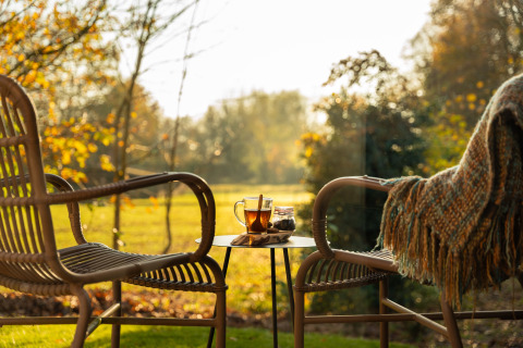 Twee rotan stoelen en een tafeltje met thee op het terras bij Wellness Duynzicht, Sandberghe, Nederland.