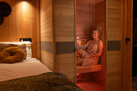 Woman relaxing in an infrared sauna next to a cozy bed at Wellness Duynzicht at Sandberghe in the Netherlands.