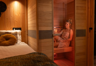 Frau entspannt in einer Infrarotsauna neben einem gemütlichen Bett in Wellness Duynzicht, Sandberghe, Niederlande.