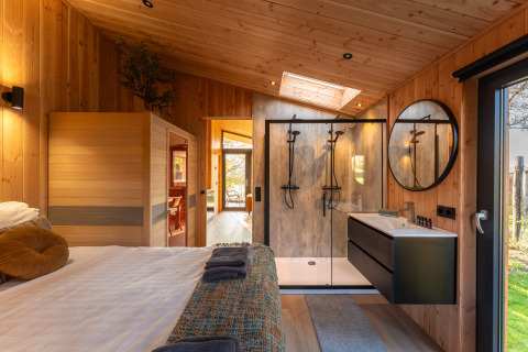 Interno di lodge moderno con pannelli in legno, letto matrimoniale, doccia e sauna a Wellness Duynzicht, Sandberghe, Paesi Bassi.