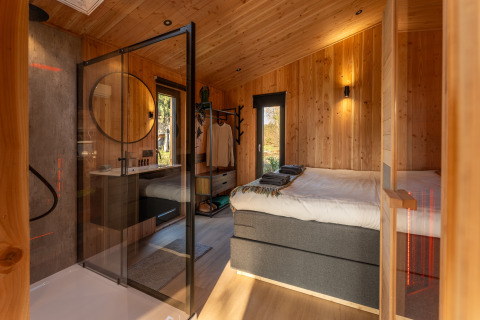 Modern lodge room at Wellness Duynzicht, Sandberghe, Netherlands, with wooden walls and glass shower area.