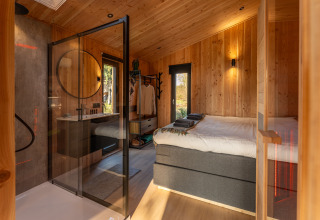 Modern lodge room at Wellness Duynzicht, Sandberghe, Netherlands, with wooden walls and glass shower area.