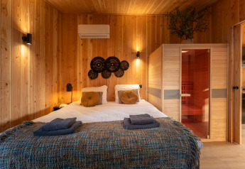Slaapkamer van Wellness Duynzicht lodge met sauna, houten wanden en tweepersoonsbed op Sandberghe, Nederland.