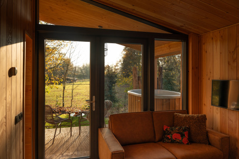 View from Wellness Duynzicht lodge at Sandberghe, Netherlands with sofa, wooden interior, and outdoor tub.