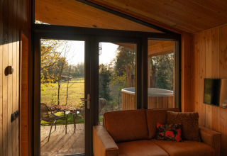 View from Wellness Duynzicht lodge at Sandberghe, Netherlands with sofa, wooden interior, and outdoor tub.