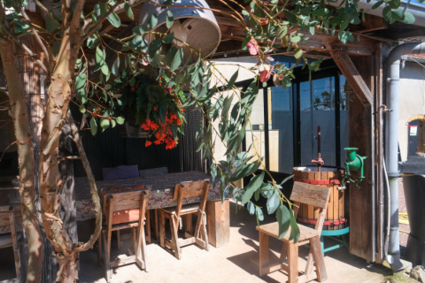 Zona de estar al aire libre con muebles rústicos de madera, flores y una prensa de vino en La Maison Bornat, Borgoña, Francia.