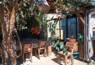 Outdoor seating area with rustic wooden furniture, flowers, and a wine press at La Maison Bornat in Burgundy, France.