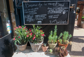 Cartel de entrada y macetas con flores en La Maison Bornat, un parque vacacional en Bourgogne-Franche-Comté, Francia.