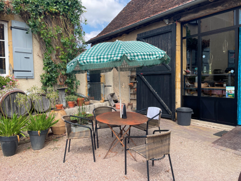 Terraza exterior con mesa redonda, tres sillas y sombrilla verde a cuadros en La Maison Bornat, Francia.