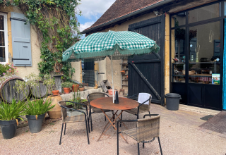 Patio esterno con tavolo rotondo, tre sedie e ombrellone a quadretti verdi a La Maison Bornat, Francia.