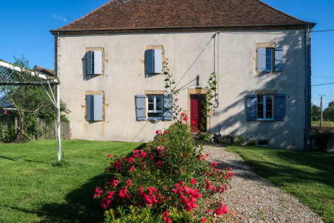 Fachada de La Maison Bornat en Bourgogne-Franche-Comté, Francia, con césped y rosales en el jardín.