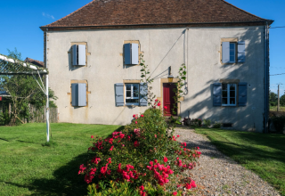 Fachada de La Maison Bornat en Bourgogne-Franche-Comté, Francia, con césped y rosales en el jardín.