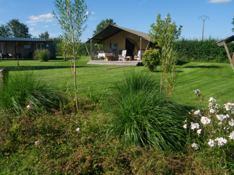 Vue sur La Maison Bornat, parc de vacances en Bourgogne, France, avec pelouse, fleurs et tente lodge.
