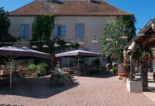 Udendørs terrasse på La Maison Bornat feriepark i Bourgogne-Franche-Comté, Frankrig, med parasoller og caféborde.