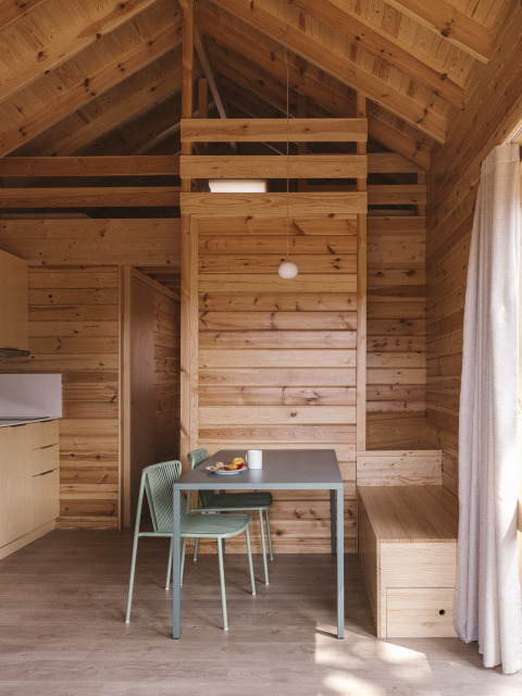 Interior de una pequeña casa de madera en Wecamp Cala Montgó, España, con mesa de comedor y ambiente cálido.