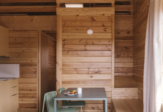 Interior de una pequeña casa de madera en Wecamp Cala Montgó, España, con mesa de comedor y ambiente cálido.