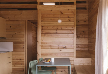 Interior de una pequeña casa de madera en Wecamp Cala Montgó, España, con mesa de comedor y ambiente cálido.
