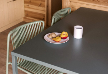 Moderner Essbereich in einem Holzbungalow mit dunklem Tisch, Stuhl, Keksen, Obst und weißer Tasse.