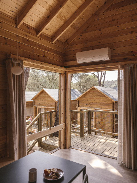 Vista interior de una pequeña cabaña de madera con terraza y otras cabañas en Wecamp Cala Montgó, España.