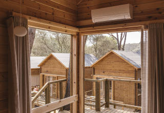 Vista interior de una pequeña cabaña de madera con terraza y otras cabañas en Wecamp Cala Montgó, España.