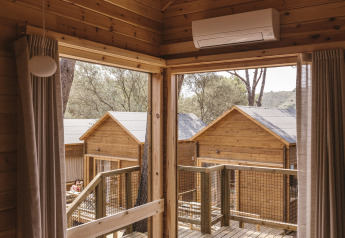 Vista interior de una pequeña cabaña de madera con terraza y otras cabañas en Wecamp Cala Montgó, España.
