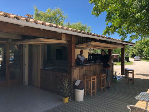 Outdoor café bar at Campsite Les Franquettes in Nouvelle-Aquitaine, France, with two staff members behind the counter.